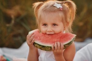 Child eating watermelon in the garden. Kids eat fruit outdoors. Healthy snack for children. Little