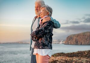 Lovely senior couple standing on the rocks at sea enjoying nature and freedom looking the horizon