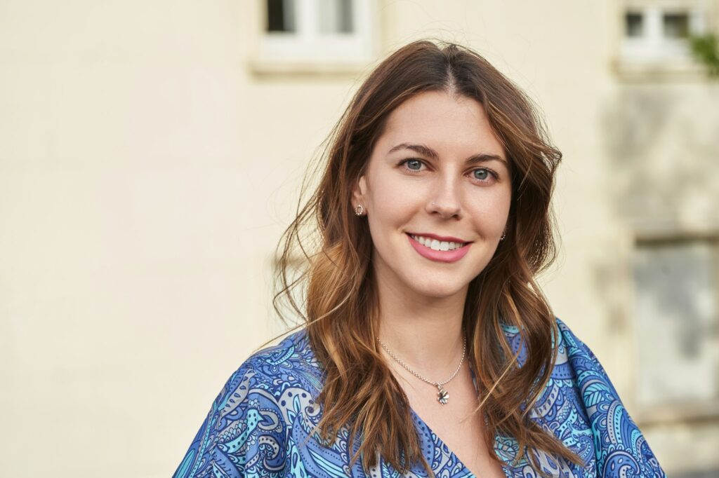 Portrait of a woman smiling at the camera while standing outdoors on the street.