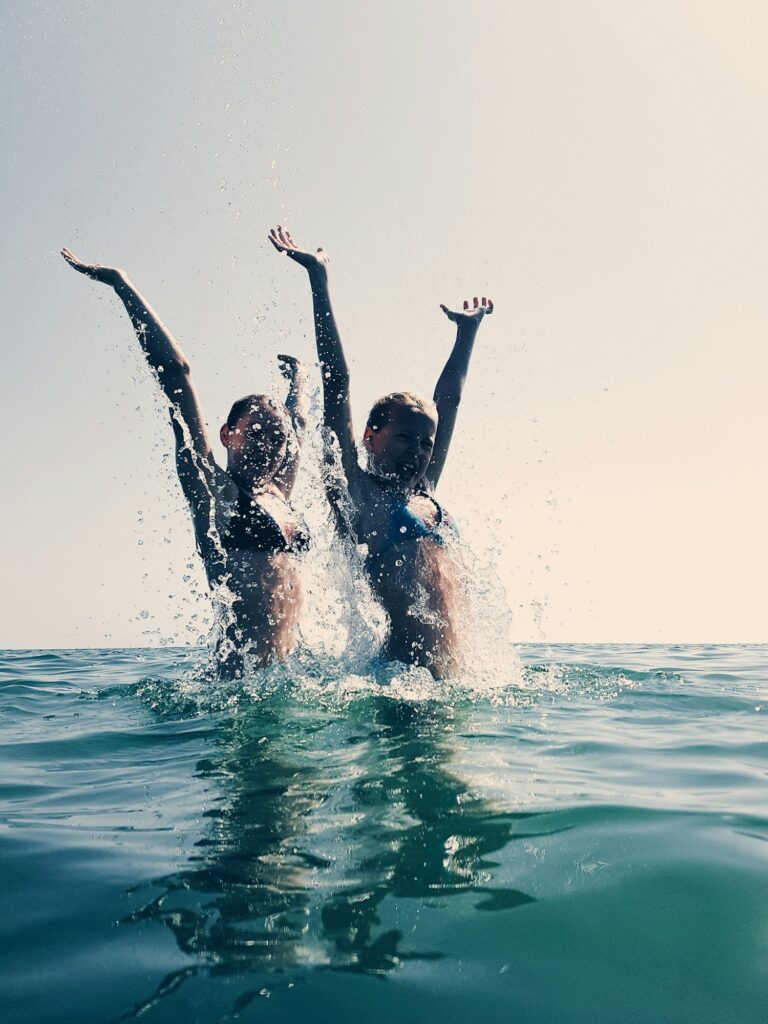 Two girls having fun in the ocean. Jumping and splashing water.