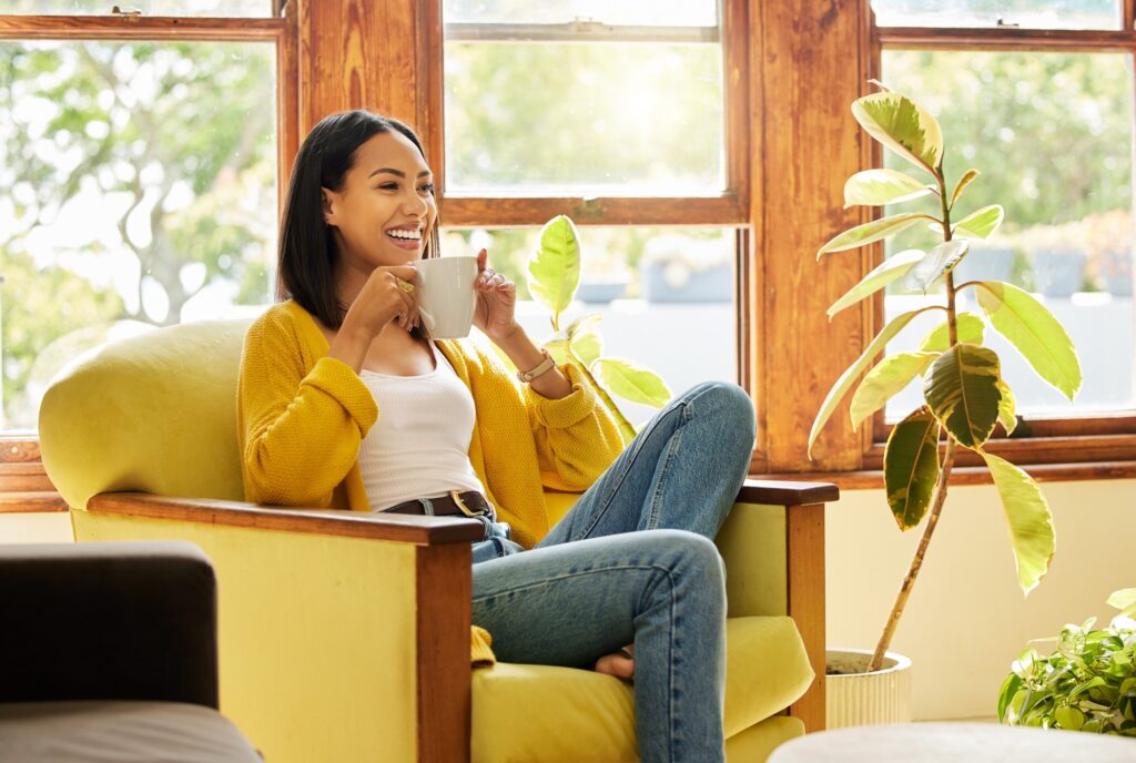 Woman relaxing, drinking coffee sitting in front of a window in a bright living room. A happy smili