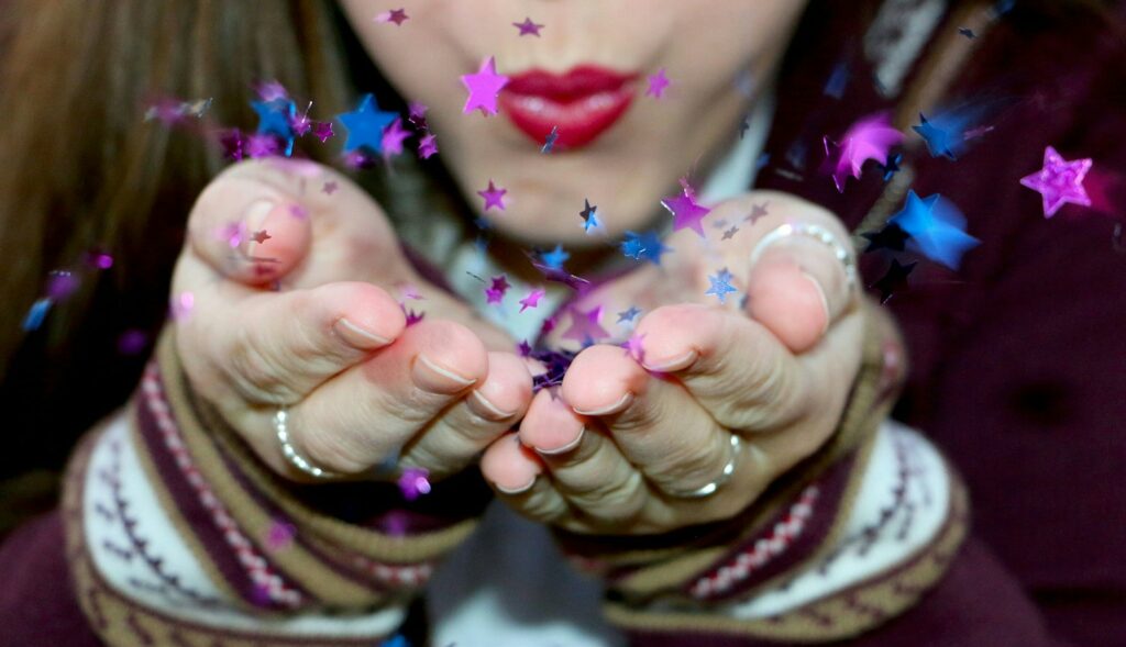 Young woman blowing star shaped confetti from her hands.